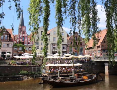 Historische Gebäude und Cafés an einem Flussufer mit einem alten Boot im Vordergrund.