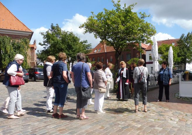 Gruppe von Menschen bei einer Stadtführung in Wesselburen auf einem gepflasterten Platz.