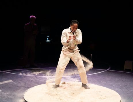A person stands on sand and pours sand in a circular motion from a bottle.