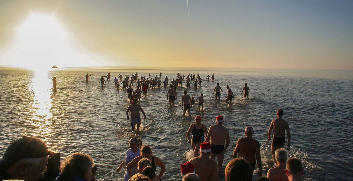 Menschenmengen beim Neujahrsanbaden im Meer bei Sonnenaufgang.