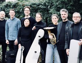 Gruppe von acht Personen mit Musikinstrumenten im Freien.