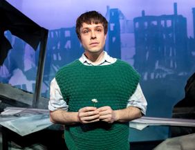 Ein junger Mann (Severin Mauchle) im grünen Pullunder, hält eine kleine weiße Blume in der Hand.