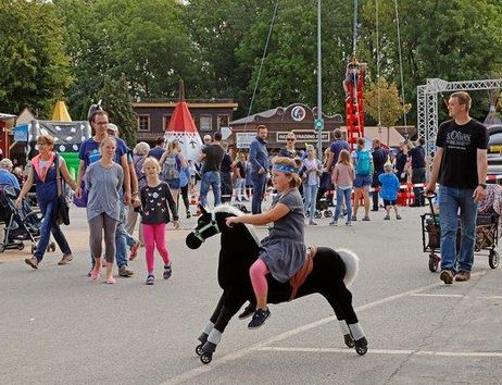 A cheerful folk festival with many people and stalls. A child rides on a toy horse and attracts the attention of passersby.