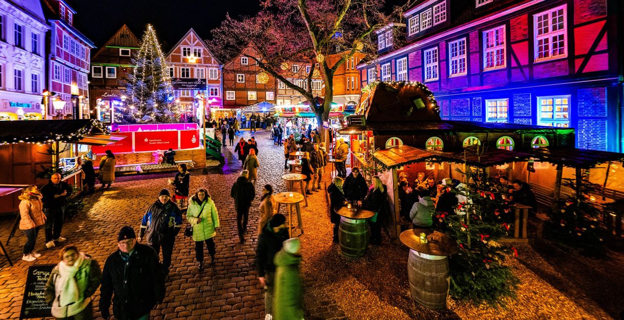 Weihnachtsmarkt mit Menschen, Lichtern und geschmückten Tannenbäumen.
