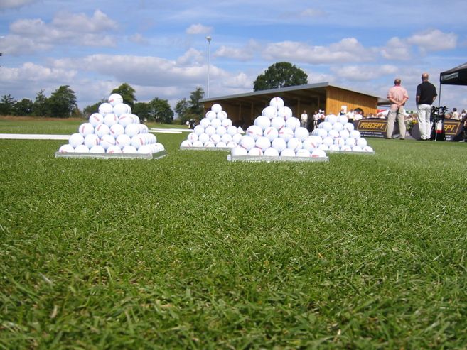 Golfbälle in Pyramidenform auf einer Driving Range mit Personen im Hintergrund.