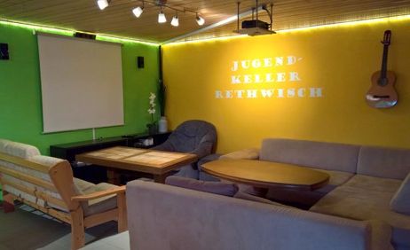 Gemütlicher Raum mit Sofas, Tisch, Leinwand und Gitarre an der Wand.