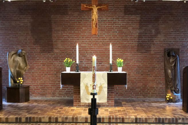 Kirchenaltar mit Kreuz, Kerzen und Blumen.
