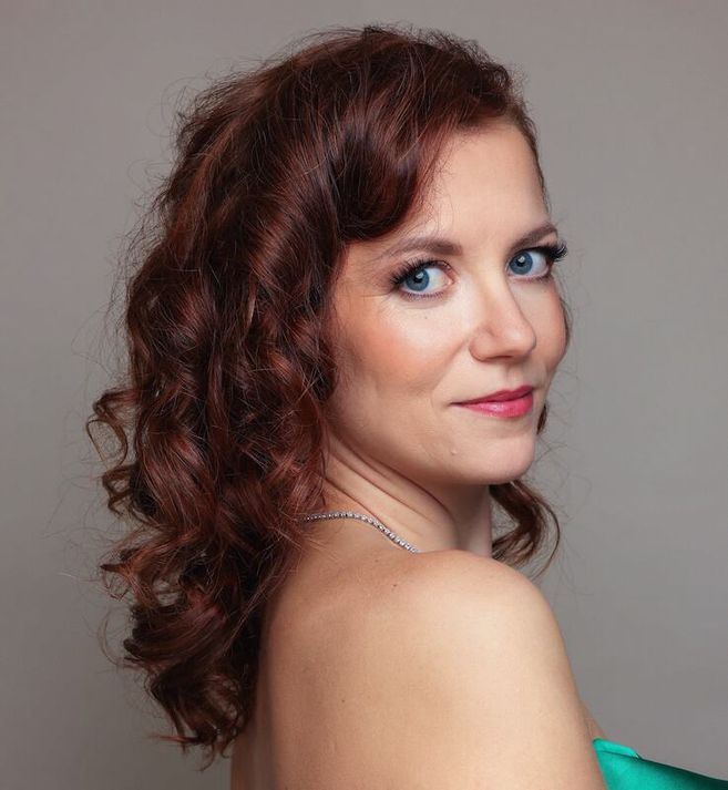 Porträt einer Frau mit lockigem, rotem Haar und blauem Kleid, die über die Schulter schaut.