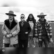 Vier Männer in unterschiedlicher Kleidung stehen auf einem Feld.