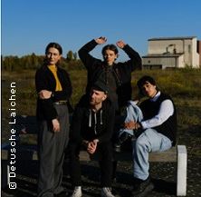 Vier Personen posieren auf einer Bank in einer ländlichen Umgebung mit einem Gebäude im Hintergrund.