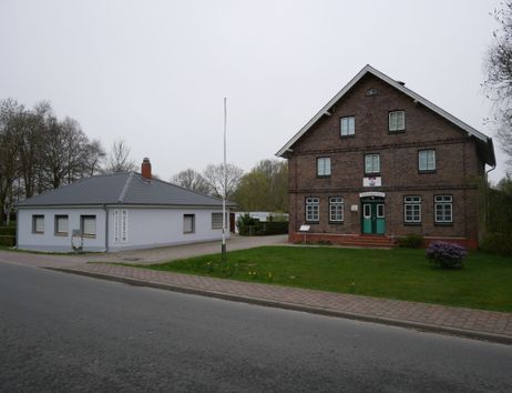 Ein kleines Museum und ein größeres Backsteingebäude an einer Straße.