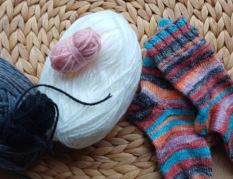 Verschiedene Wollknäuel und gestrickte Socken auf einem geflochtenen Untersetzer.
