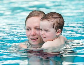 Eine Frau hält ein Kleinkind im Wasser eines Schwimmbeckens.