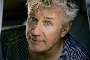 Ein Mann mit grauen Haaren und blauem Pullover schaut freundlich in die Kamera.