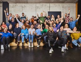 Eine Gruppe von Menschen sitzt auf einer Holztribüne und jubelt fröhlich in die Kamera.