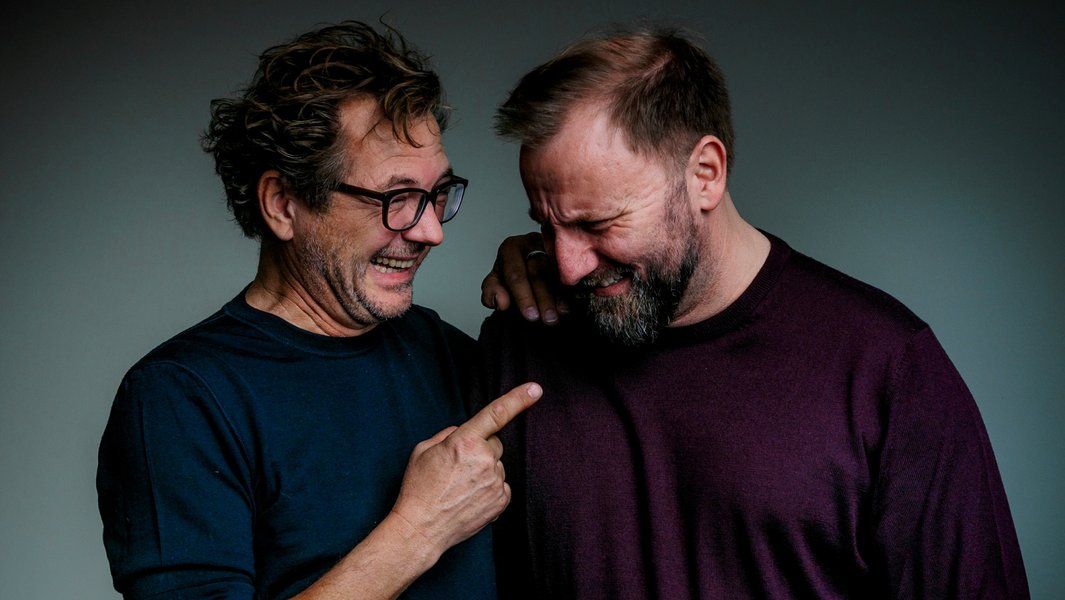 Zwei Männer lachen herzlich, einer zeigt auf den anderen.