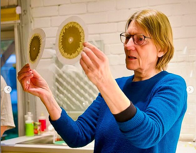 Eine Frau in einem blauen Pullover hält zwei runde, kunstvolle Objekte in den Händen.