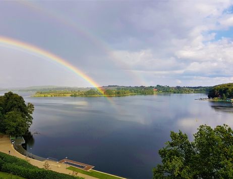 A beautiful lake with a rainbow and a calm water surface. The landscape is surrounded by trees and conveys a peaceful atmosphere.
