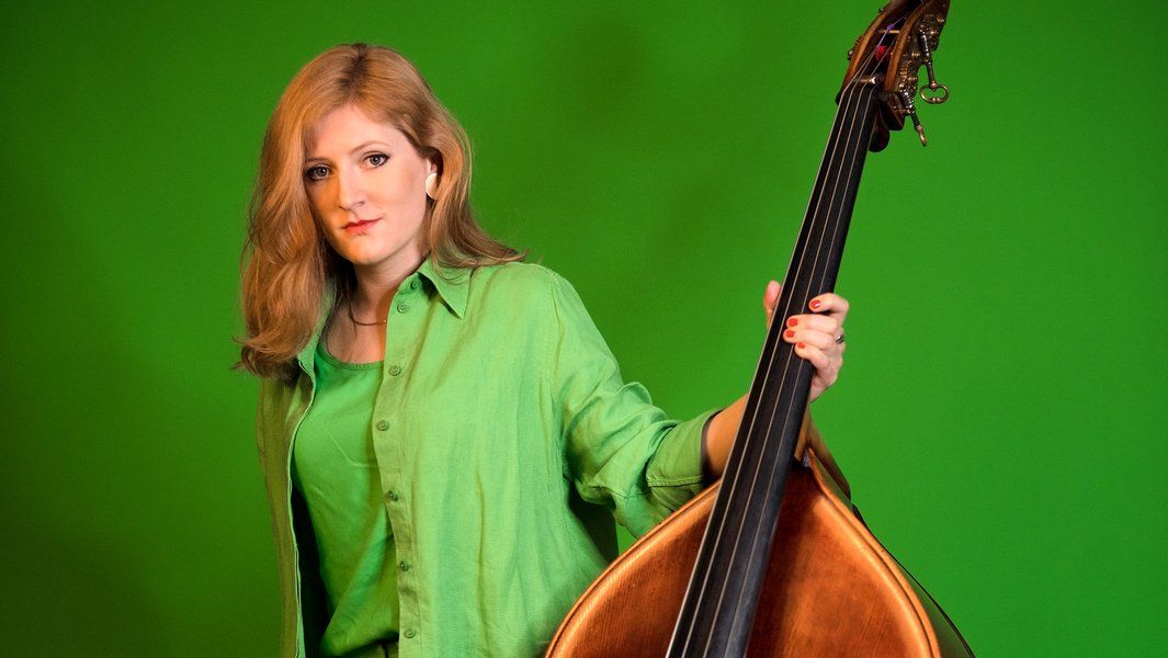Eine Frau in grüner Kleidung hält einen Kontrabass vor einem grünen Hintergrund.