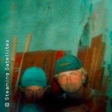 Zwei Personen mit Mützen vor einer Wand mit Holzplanken.