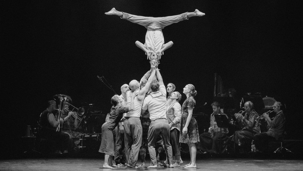 Akrobaten führen eine Menschenpyramide auf, während ein Orchester im Hintergrund spielt.
