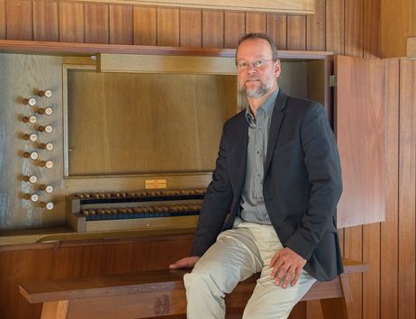 Ein Mann sitzt auf einer Orgelbank vor einer hölzernen Orgel.