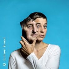 Eine Frau hält ein Porträt eines älteren Gesichts vor ihr eigenes, vor blauem Hintergrund.