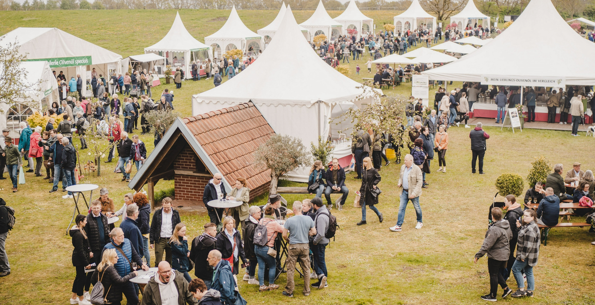 Menschenmenge bei den Oliven-Abholtagen in Wilstedt mit weißen Zelten und Ständen auf einer Wiese.