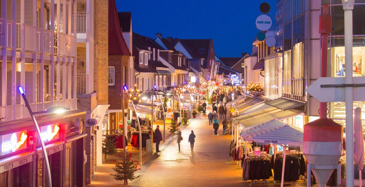 Eine belebte Einkaufsstraße in Büsum bei Nacht, festlich beleuchtet mit Weihnachtsdekorationen und Menschen, die entlang der Geschäfte schlendern.