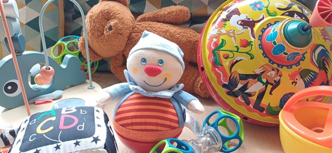 Spielzeug und Kuscheltiere in einer Krabbelgruppe: ein Stoffclown, ein Teddybär und buntes Babyspielzeug auf dem Boden.
