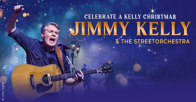 Jimmy Kelly spielt Gitarre und singt auf einer Bühne mit Lichtern im Hintergrund.