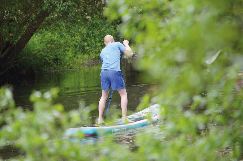 Person beim Stand-up Paddling auf einem Fluss, umgeben von grüner Vegetation.