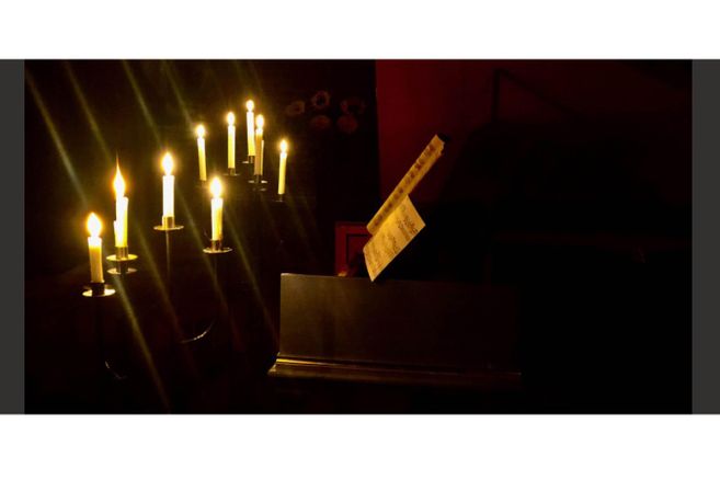 Ein Klavier mit Notenblatt, beleuchtet von mehreren brennenden Kerzen in einem dunklen Raum.