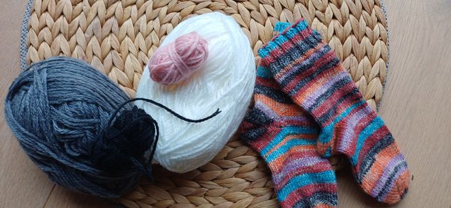 Verschiedene Wollknäuel und gestrickte Socken auf einem geflochtenen Untersetzer.