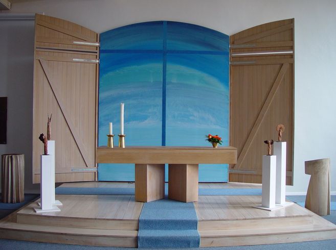 Moderner Kirchenaltar mit Holztisch, Kerzen und blauer Hintergrundgestaltung.
