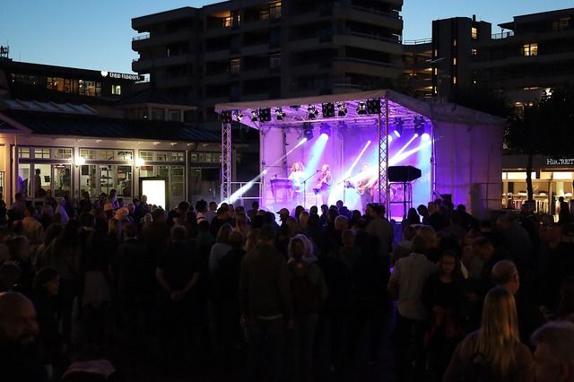 Menschenmenge bei einem Konzert im Freien bei Nacht mit beleuchteter Bühne.