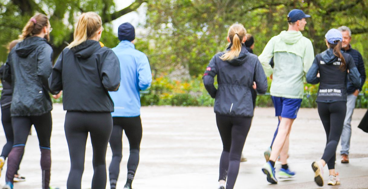Eine Gruppe von Menschen joggt durch einen Park mit Bäumen im Hintergrund.