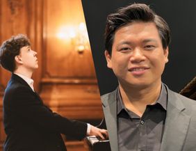 Zwei Männer in formeller Kleidung, einer spielt Klavier, der andere lächelt in die Kamera.