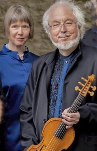 Ein Mann mit weißem Bart hält eine Geige, neben ihm steht eine Frau. Beide tragen blaue Kleidung.