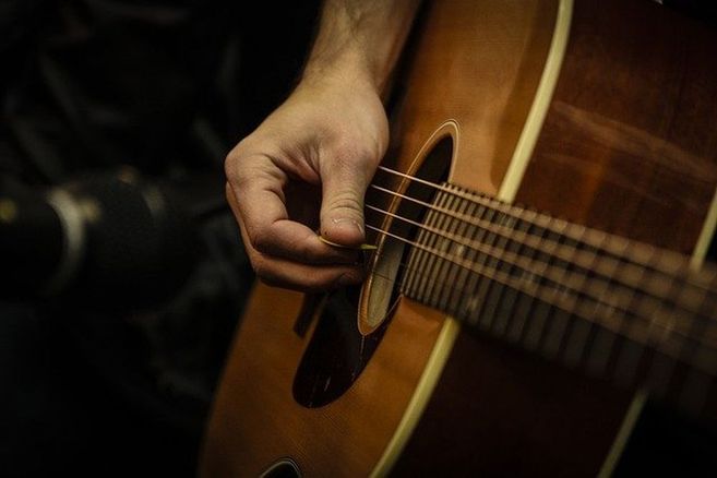 Nahaufnahme einer Hand, die eine Akustikgitarre spielt.