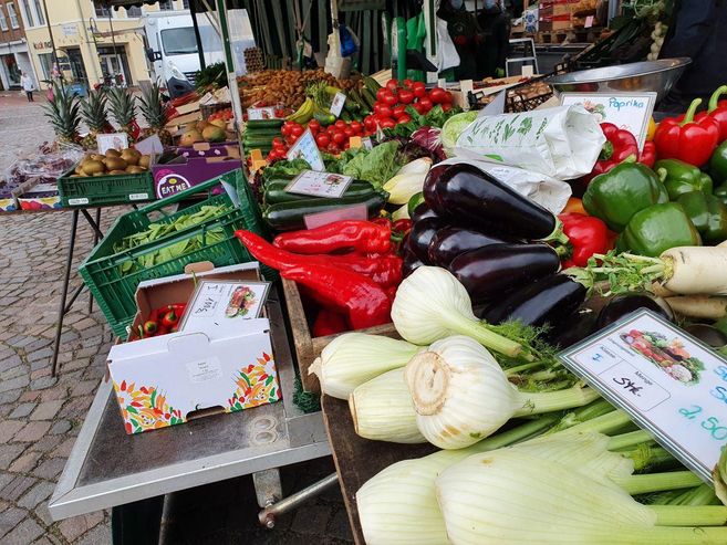 Ein Marktstand mit frischem Gemüse wie Paprika, Auberginen und Fenchel auf einem Wochenmarkt.