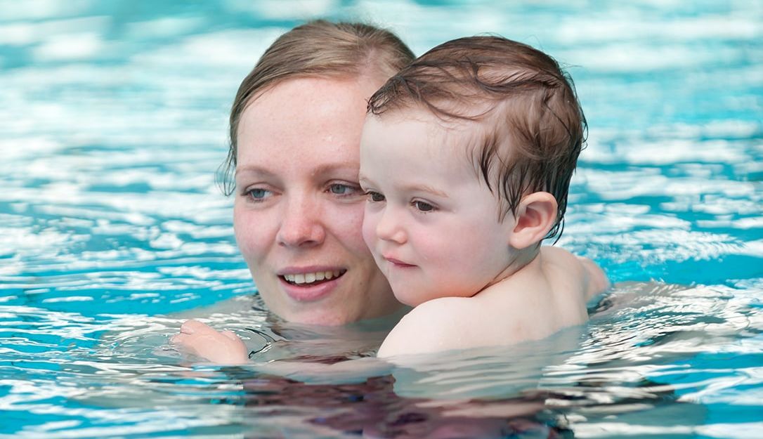 Eine Frau hält ein Kleinkind im Wasser eines Schwimmbeckens.