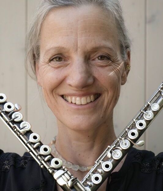 Frau mit zwei Querflöten vor hellem Hintergrund.