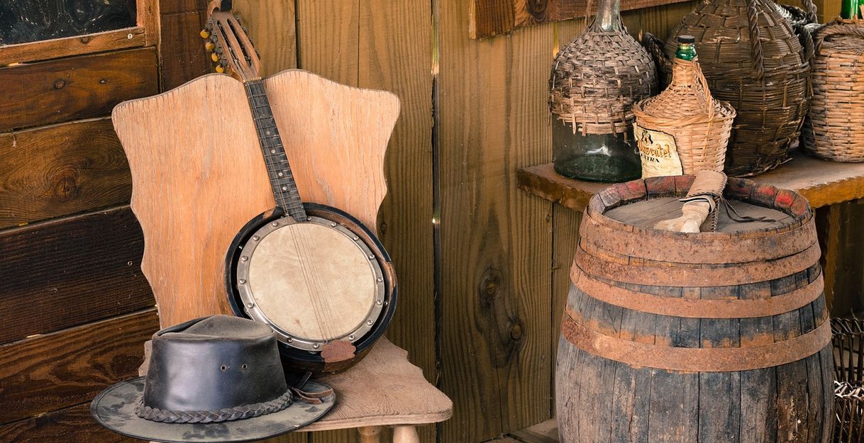 Banjo und Hut auf einem Stuhl. Daneben ein altes Fass und große Flaschen