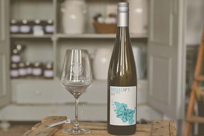 Weinflasche und Glas auf einem Holztisch vor einem Regal.