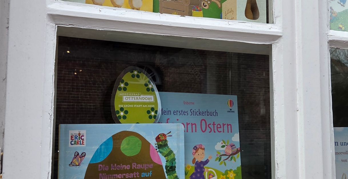 Ein Schaufenster mit Osterbüchern und Dekorationen, darunter Plüschhasen und bunte Kinderbücher.