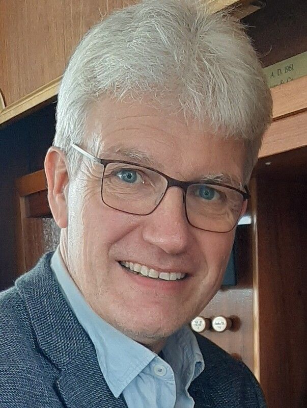 Porträt eines lächelnden Mannes mit Brille und grauem Haar.