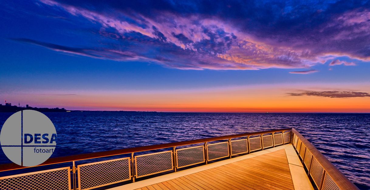 Seebrücke mit Blick auf das Meer bei Sonnenaufgang, der Himmel ist in Blau- und Orangetönen gefärbt.