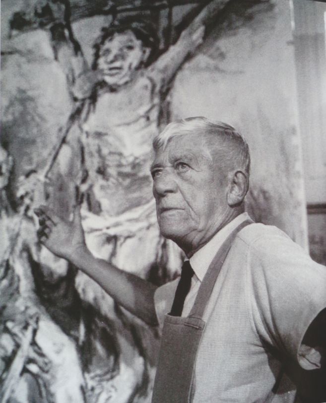 Ein älterer Mann steht vor einem großen Gemälde und gestikuliert mit der Hand.