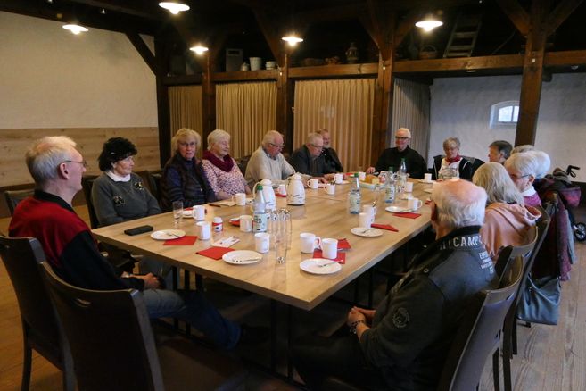 Eine Gruppe älterer Menschen sitzt um einen Tisch in einem Raum mit Holzbalken.